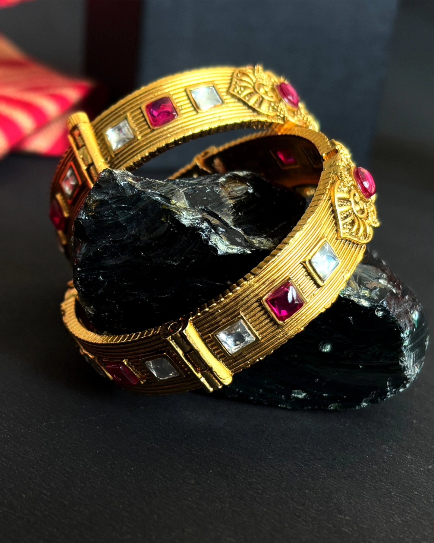 Gold kundan bangles with ruby and clear stones, styled on black stone